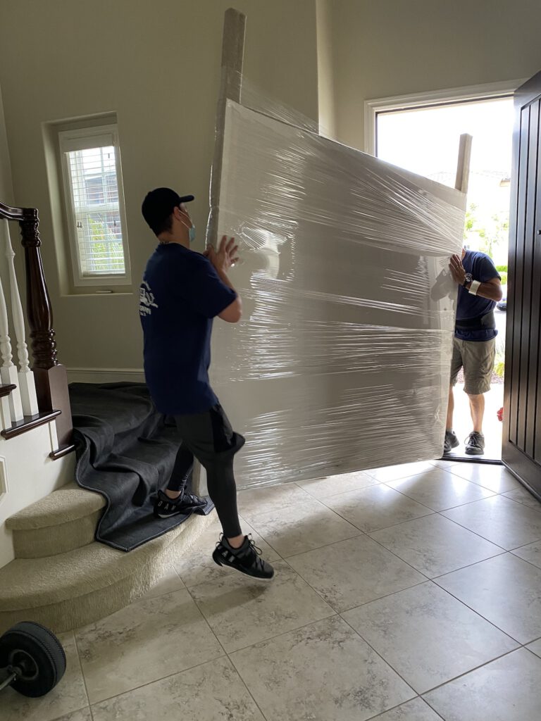 Strong professional Movers move a large headboard out the door