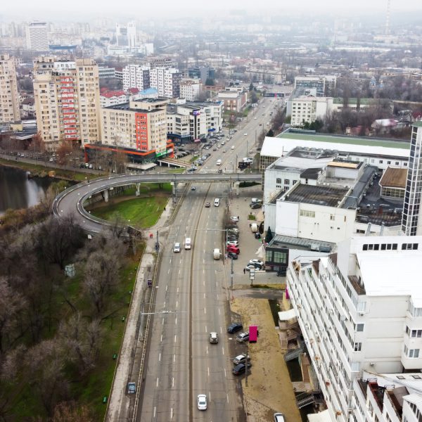 Aerial drone panorama view of Chisinau, street with multiple residential and commercial buildings, road with moving cars, lake with bare trees